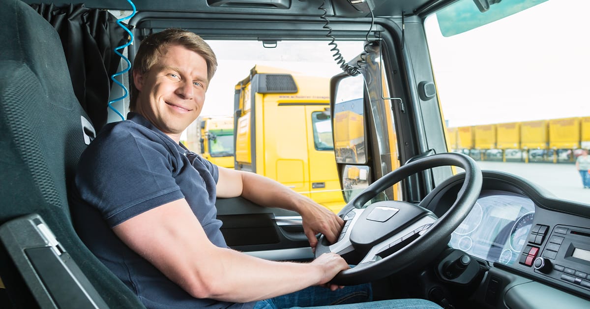 smiling-truck-driver-reducing-stress-isaac-drivewyze Professional truck driver smiling in the cab, representing reduced driver stress and improved retention through smart fleet tools and real-time safety technologies from ISAAC and Drivewyze.